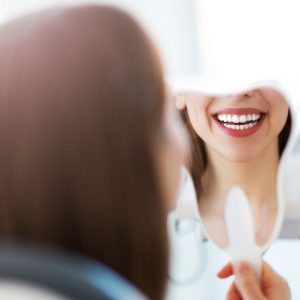 young woman smiling while holding up a hand mirror