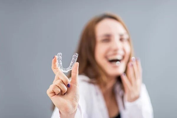 lady smiling while holding a clear aligner tray